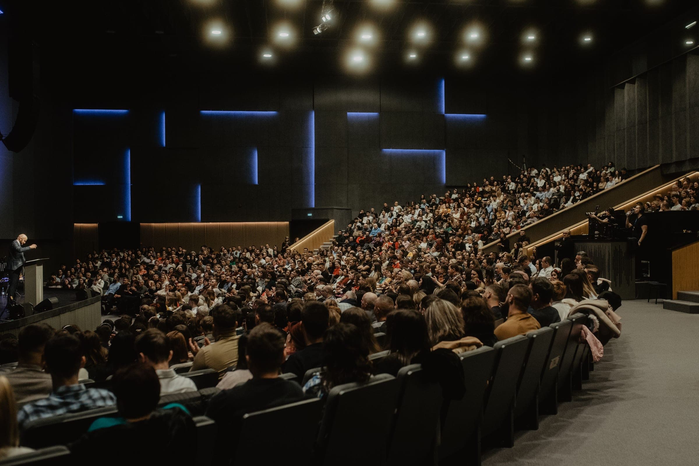 A full conference auditorium with delegates seated in tiers and a speaker at the lectern