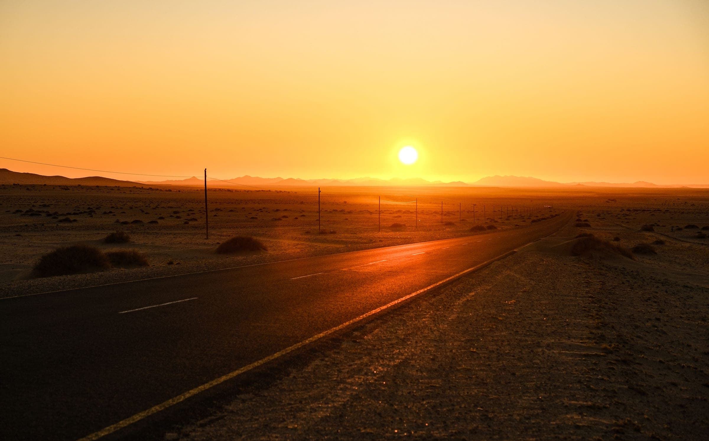 An empty two-lane desert highway running to the horizon at sunrise, the road a city-to-city chauffeur journey leaves on