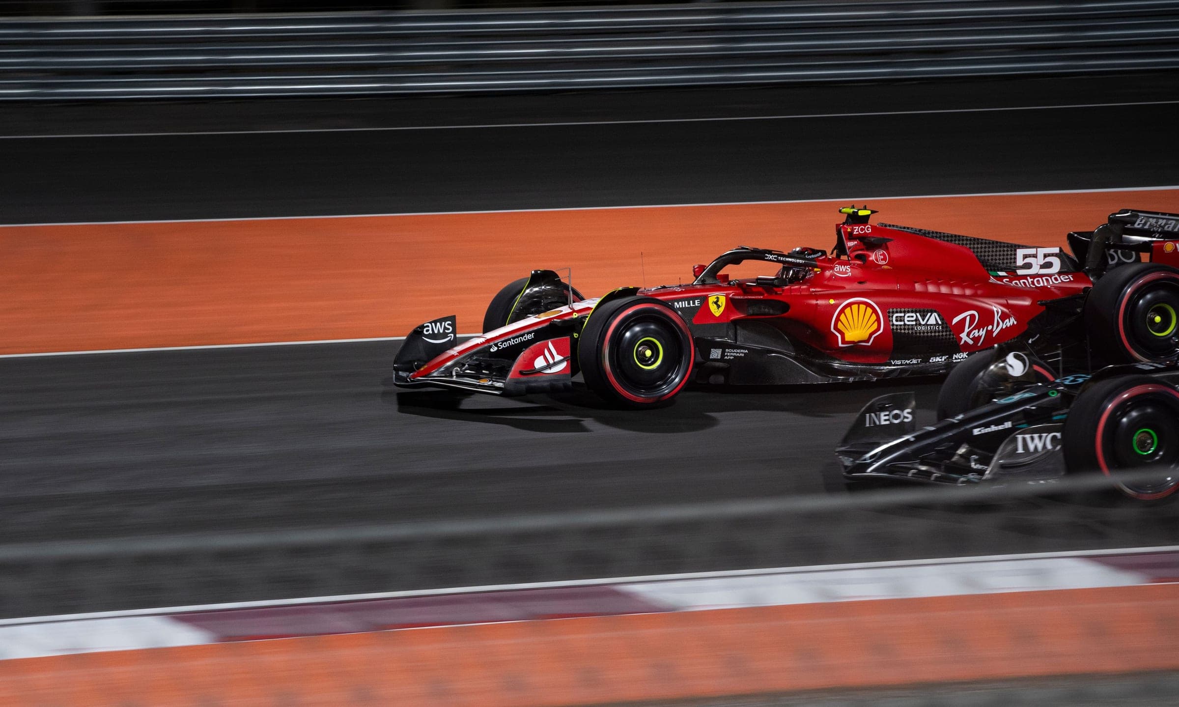 Two Formula 1 cars at speed under floodlights on a night circuit, the race-week timing an event fleet works to