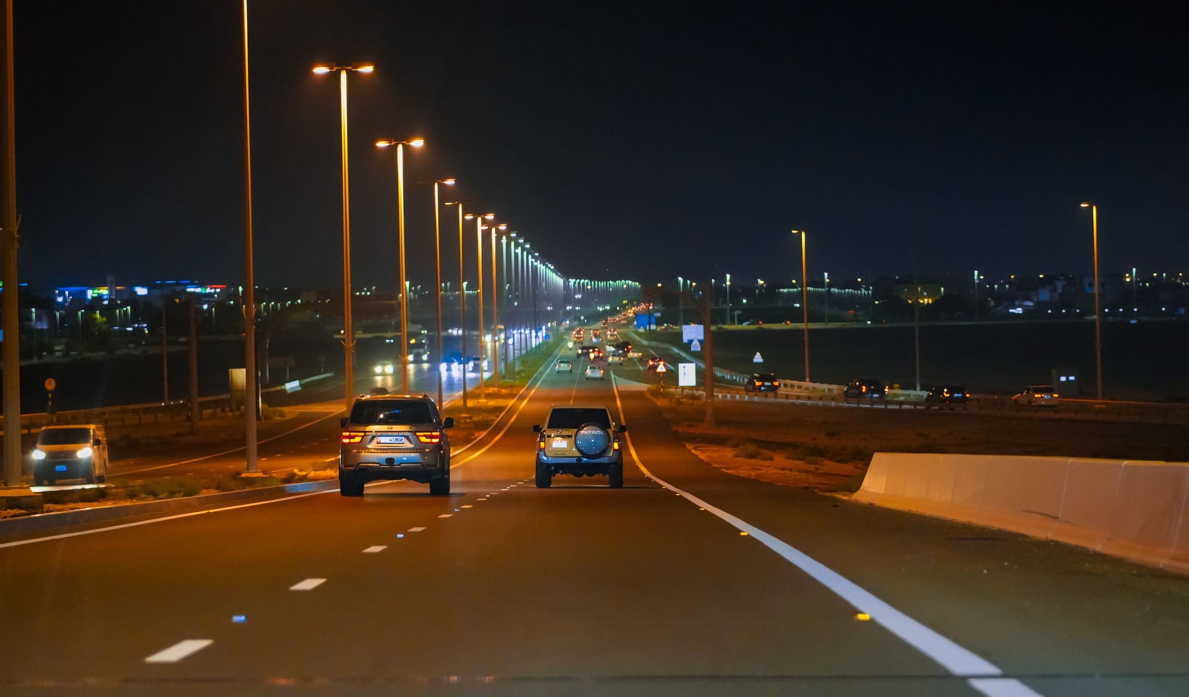 Two SUVs on a lit Gulf highway at night, the road that carries a crossing out of Saudi Arabia