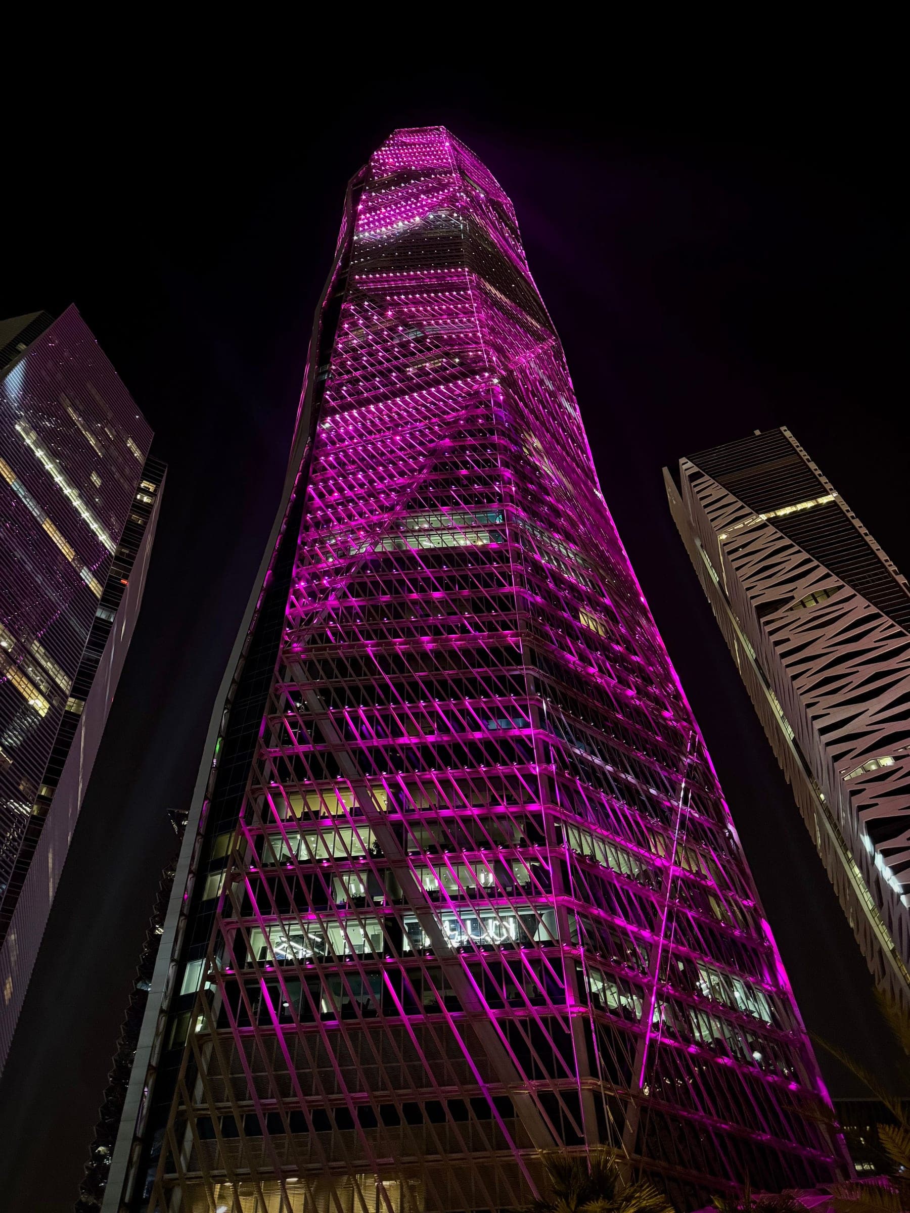 A diagrid tower in Riyadh's King Abdullah Financial District lit at night, the quarter the city's summit weeks gather around