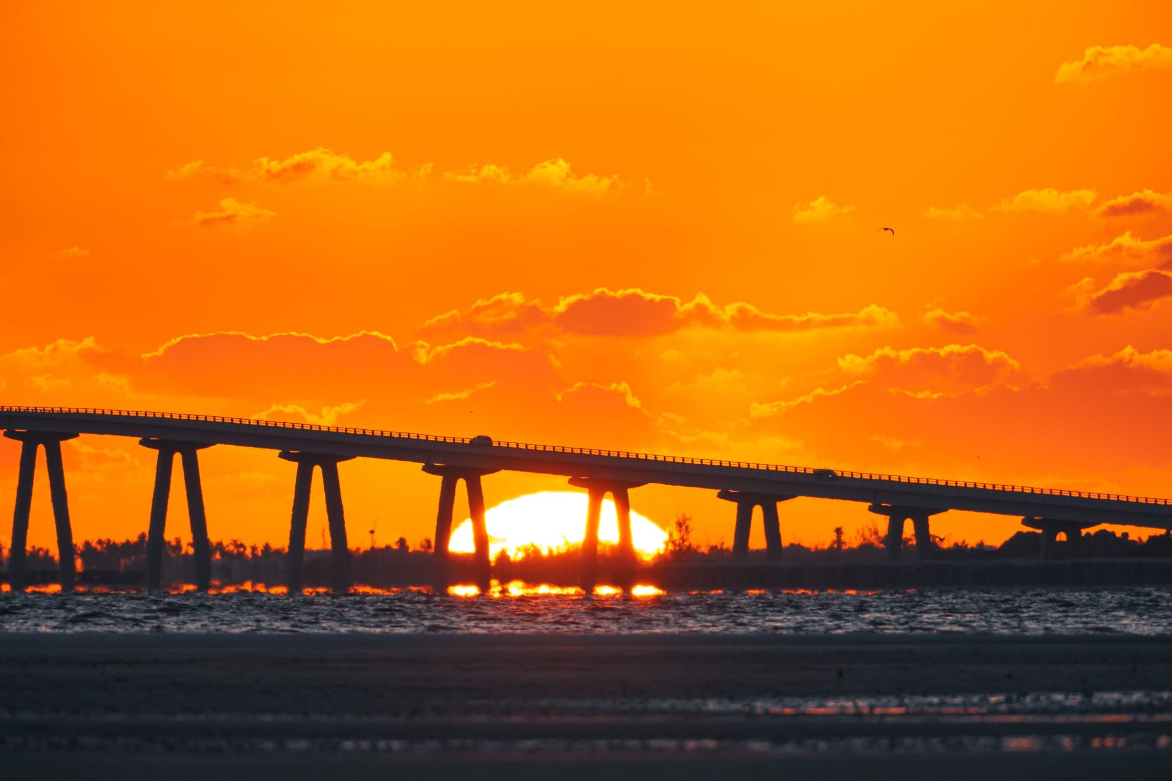 A low causeway on piers running out across the water at sunset, a single car crossing it