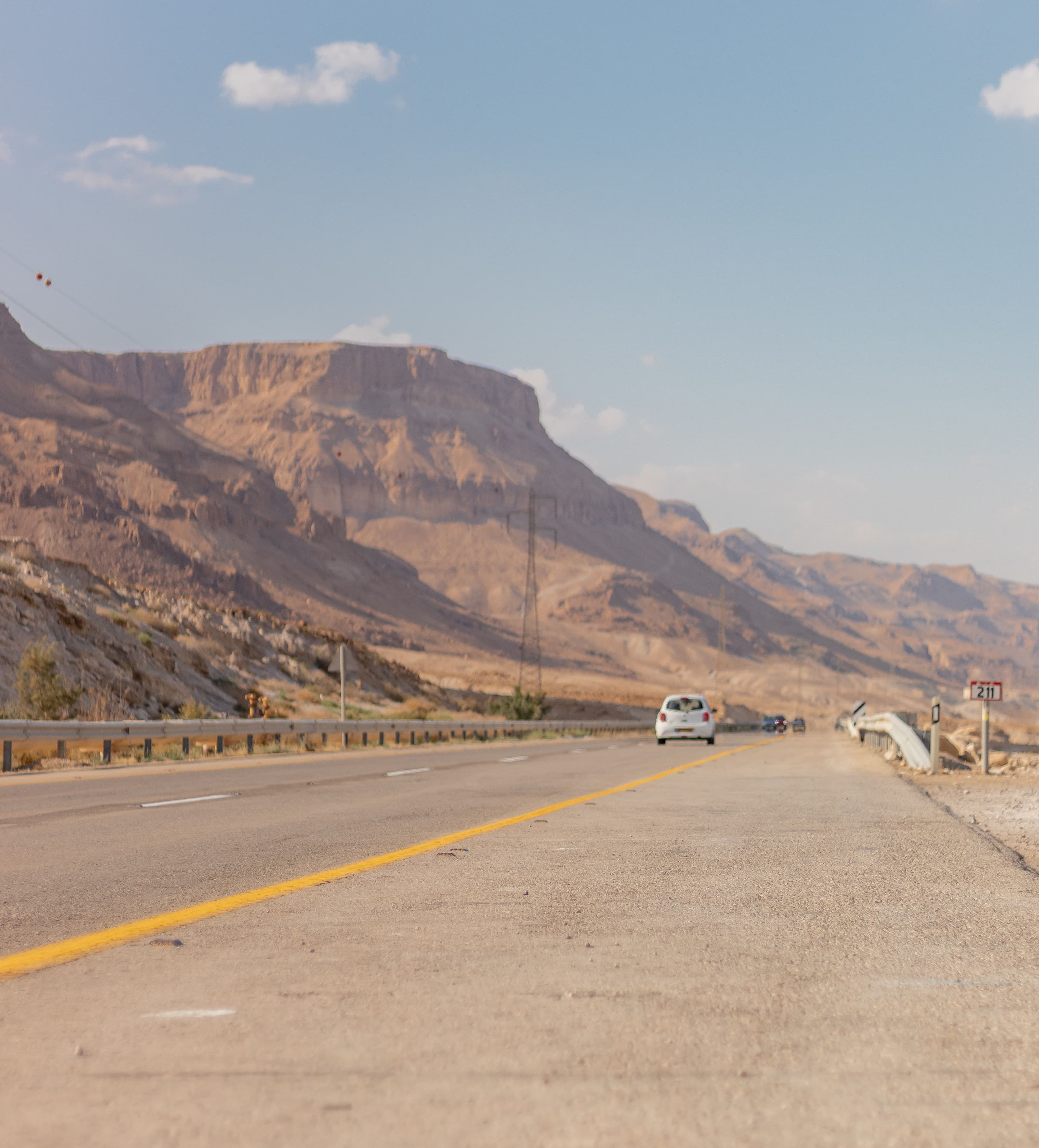 A long desert highway running below an escarpment, the road an intercity chauffeur journey is driven on