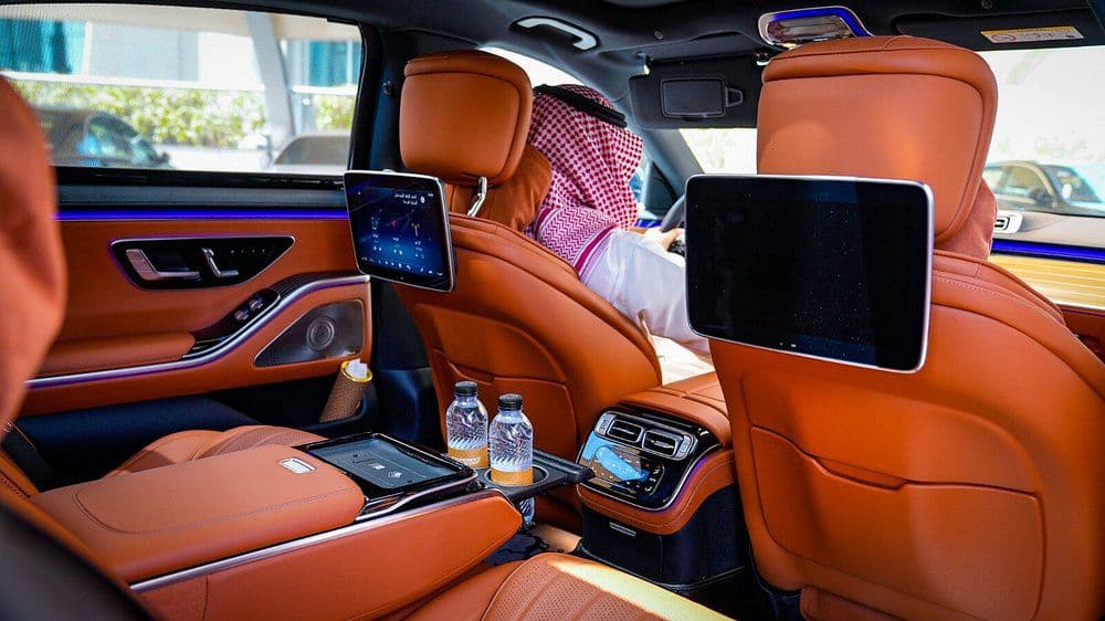 A guest seated in the rear cabin of a chauffeured S-Class with water and screens already set