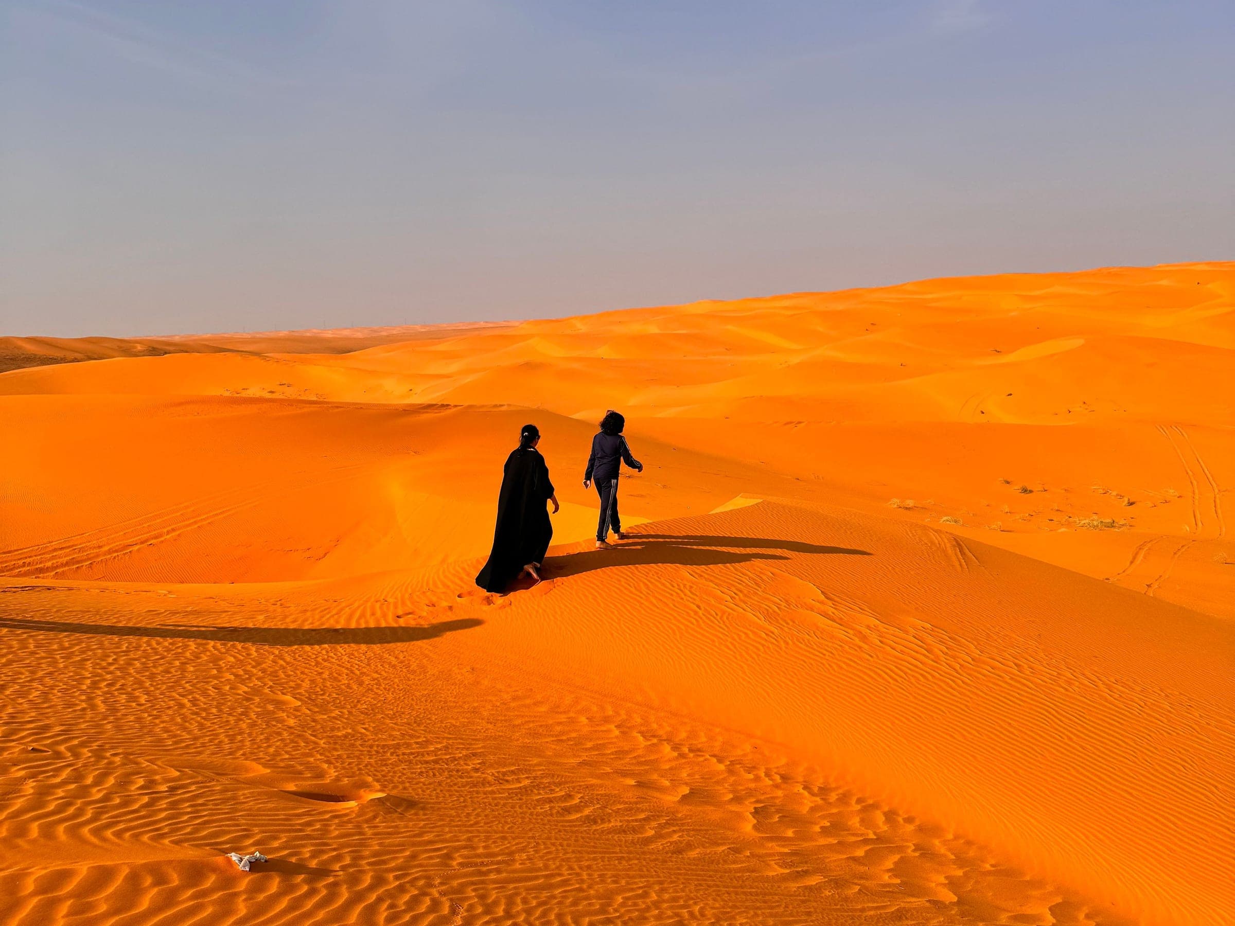 Two figures walking the red sand dunes at golden hour in Saudi Arabia, the short desert run out of Riyadh