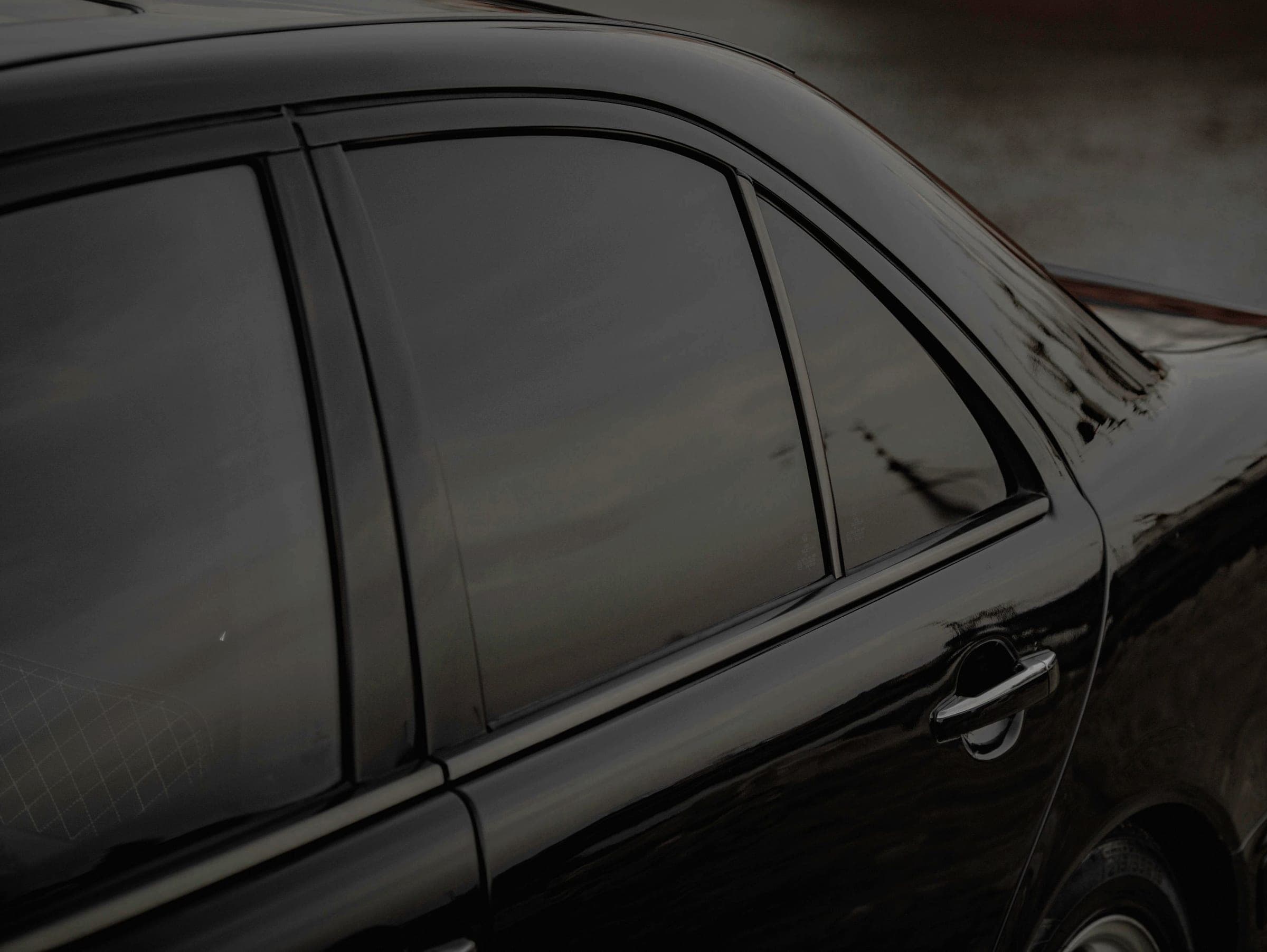 The tinted rear window and door of a black sedan, nothing visible through the glass