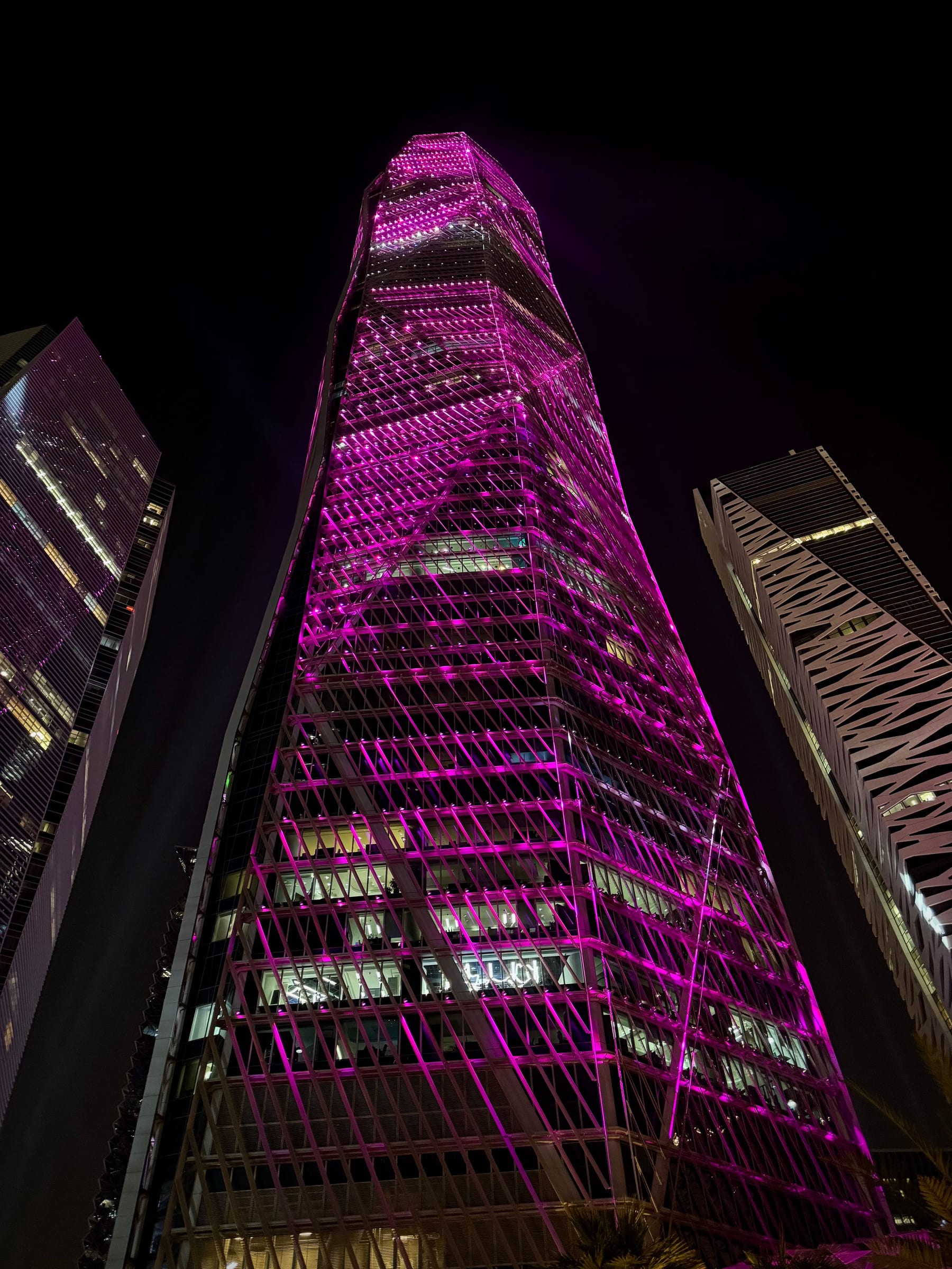 A diagrid tower in Riyadh's King Abdullah Financial District lit at night, the quarter the city's summit weeks gather around