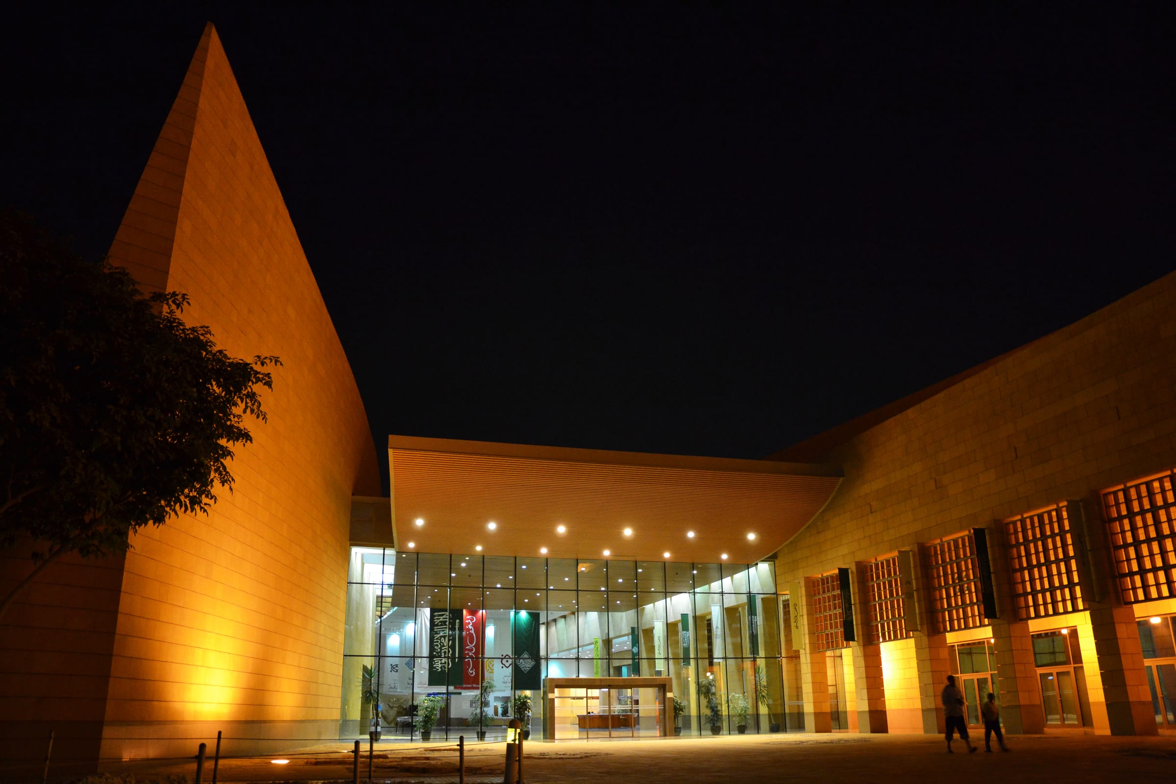 The National Museum of Saudi Arabia in Riyadh at night, the glass entrance lit under the sandstone wall of the King Abdulaziz Historical Centre